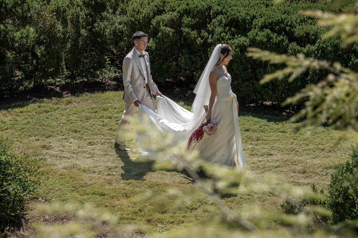 Groom carrying the bride's train through a garden